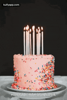 a pink birthday cake with candles and sprinkles on a white plate .