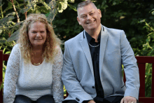 a man and a woman sit on a red bench and smile for the camera