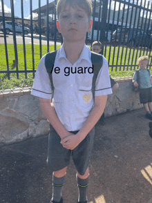 a boy wearing a white shirt and grey shorts has the word guard written on his shirt