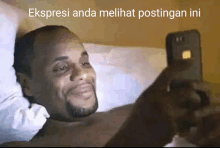 a man laying on a bed looking at a cell phone with ekspresi anda melihat postingan ini written above him