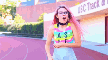 a girl with pink hair is running in front of the usc track and field building