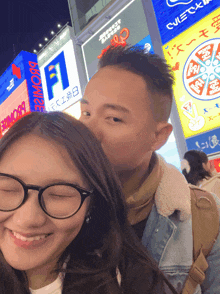 a man kisses a woman on the cheek in front of a billboard that says ' a ' on it