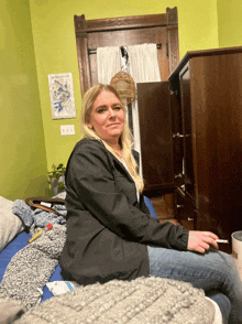 a woman in a black jacket is sitting on a bed smoking a cigarette