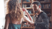 a man and a woman are standing next to each other in front of a bookshelf in a living room .