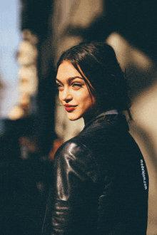 a woman wearing a black leather jacket is looking over her shoulder with a photo from modellygram.com