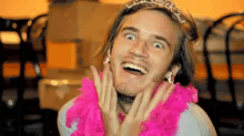 a man wearing a tiara and a pink boa is smiling and making a funny face .