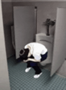 a person is bending over in a bathroom next to a urinal .