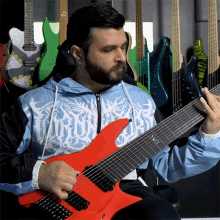 a man playing a red guitar in front of a wall of guitars including one that says ' slayer ' on it