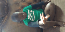 a young boy wearing a green nyc t-shirt is sitting on a couch