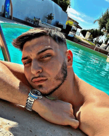 a shirtless man with a watch on his wrist is laying on the edge of a swimming pool