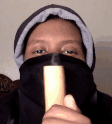 a man wearing a black scarf covering his face holds a wooden stick