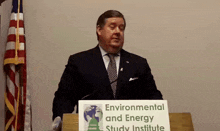 a man in a suit and tie stands behind a podium with a sign that says environmental and energy study institute