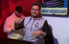 a man in a hoodie is dancing in front of a sign that says `` rogue msdossary '' .