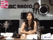 a woman is sitting at a table in front of a microphone in front of a sign that says bbc radio