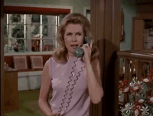 a woman in a purple dress is talking on a green telephone .