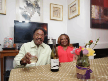 a man and a woman sit at a table with a bottle of black river wine