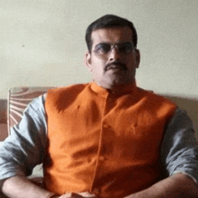 a man with a mustache and sunglasses is sitting on a couch wearing an orange vest .