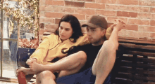 a man and a woman are sitting on a bench with a brick wall behind them