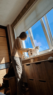 a woman petting a cat while looking out of a window