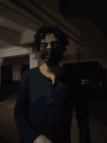 a man wearing a black mask and a blue shirt stands in a dark room