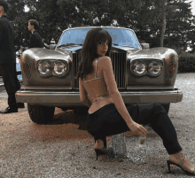 a woman is kneeling in front of a rolls royce