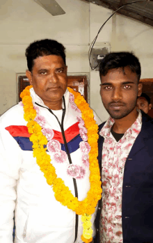 two men are posing for a picture with one wearing a garland of flowers around his neck