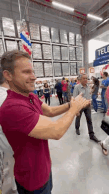 a man in a red shirt is standing in front of a crowd of people clapping their hands in a store .