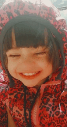 a little girl wearing a red leopard print jacket is smiling .