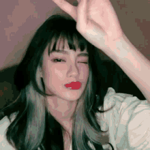 a woman with long black hair and red lips is making a heart shape with her hand .