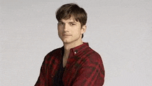 a young man wearing a red plaid shirt is standing with his arms crossed and looking at the camera .