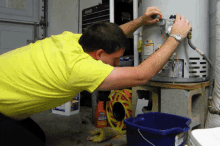 a man in a yellow shirt is working on a water heater with a bucket next to him that says aqua