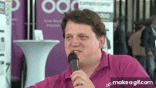 a man in a pink shirt is holding a microphone in his hand and talking into it .