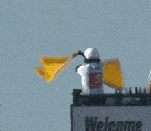 a man waves a yellow flag in front of a welcome sign