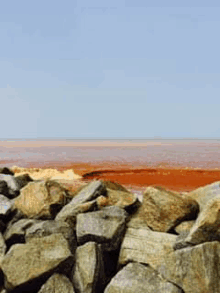 a pile of rocks sitting next to a body of water with a red ocean in the background .