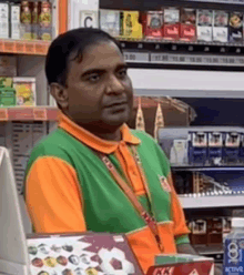 a man in a green and orange shirt is standing in front of a display of cigarettes .