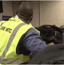 a man wearing a yellow vest with the word line mtc on it is sitting in front of a pile of luggage .