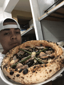 a man in a white hat is holding a pizza with asparagus on it