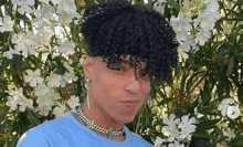 a young man with curly hair is standing in front of a tree with white flowers .