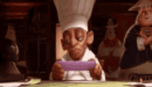 a cartoon chef is sitting at a table playing a video game on a cell phone .