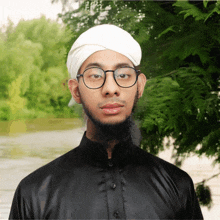 a man wearing glasses and a white turban stands in front of trees