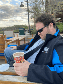 a man wearing a jacket that says tampa bay on it is holding a cup of coffee