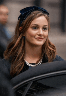 a woman wearing a headband and a pearl necklace smiles for the camera