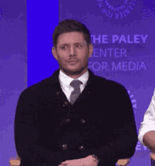 a man in a suit and tie is standing in front of a sign that says the paley center for media