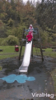 a girl in a red raincoat is laying on the ground in front of a slide in a park ..