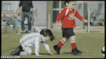 two young boys are playing soccer on a field and one is wearing a red jersey with the letter k on it .