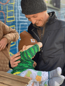 a man is holding a baby wearing a carhartt hat