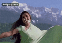 a woman in a green dress is flying in the air in front of a mountain range .