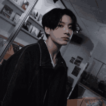 a young man wearing a black jacket and earrings is standing in front of a bookshelf .