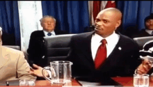 a man in a suit and tie sits at a table with a pitcher of water in front of him