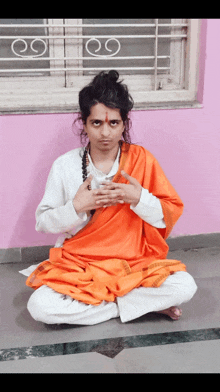 a man in a white shirt and orange robe is sitting on the floor